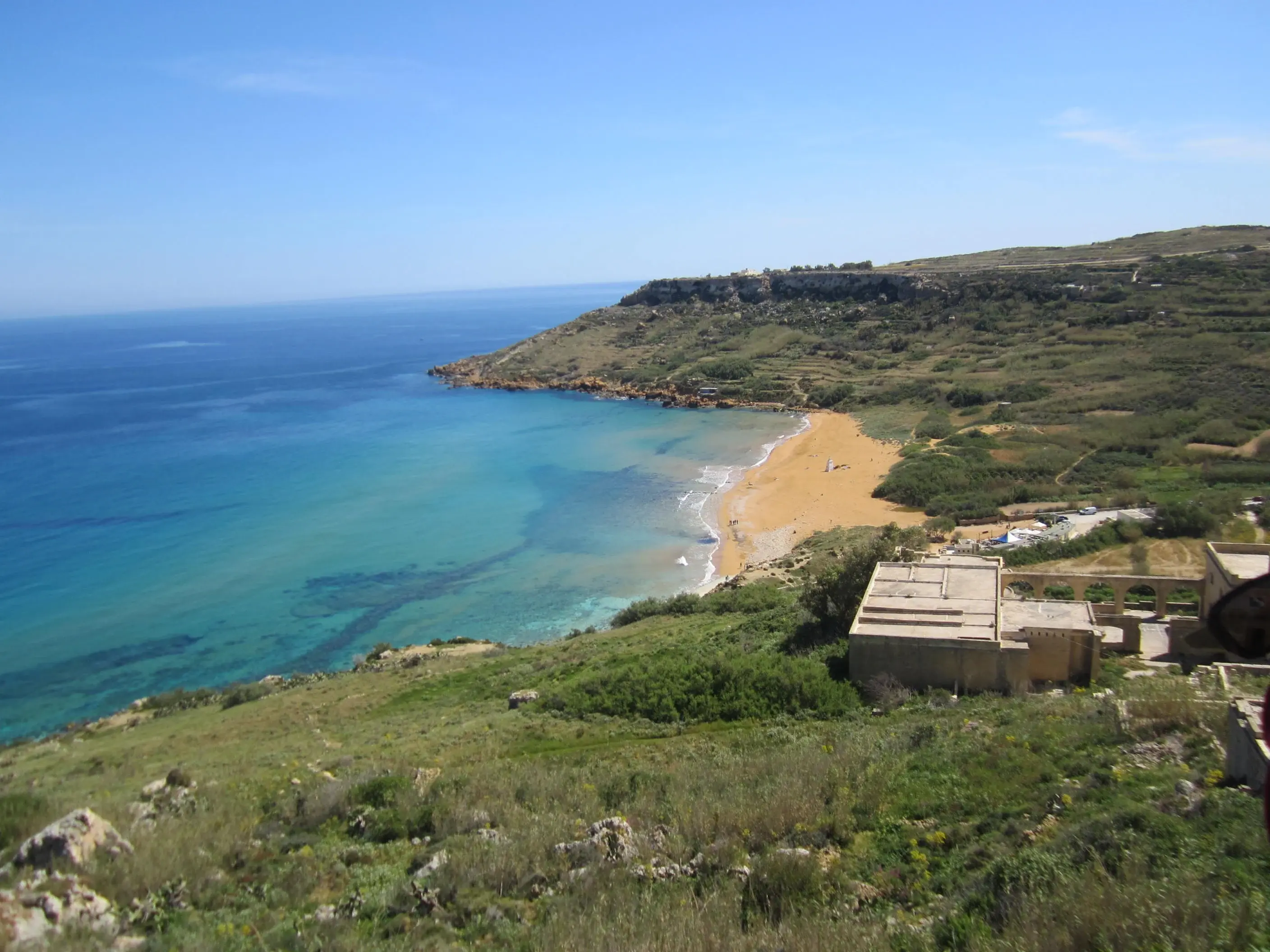 Red sand curving around turquoise water beneath the hills at Ramla Bay