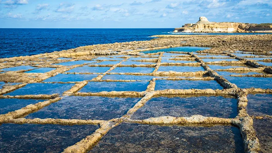 Seawater pools cut into the limestone coast beside the blue sea at Xwejni
