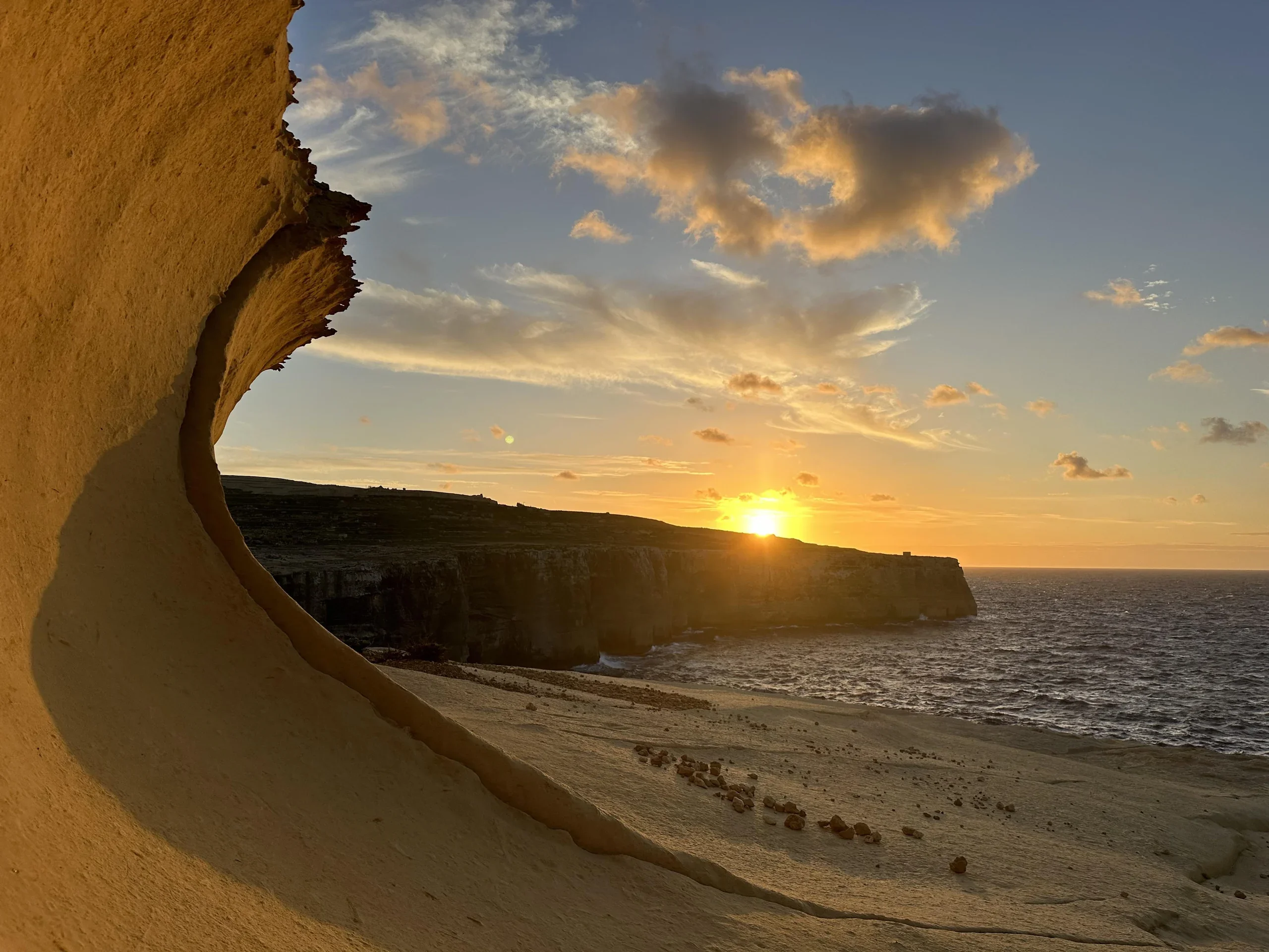 Golden sunset over coastal cliffs and the sea, framed by a curved limestone formation