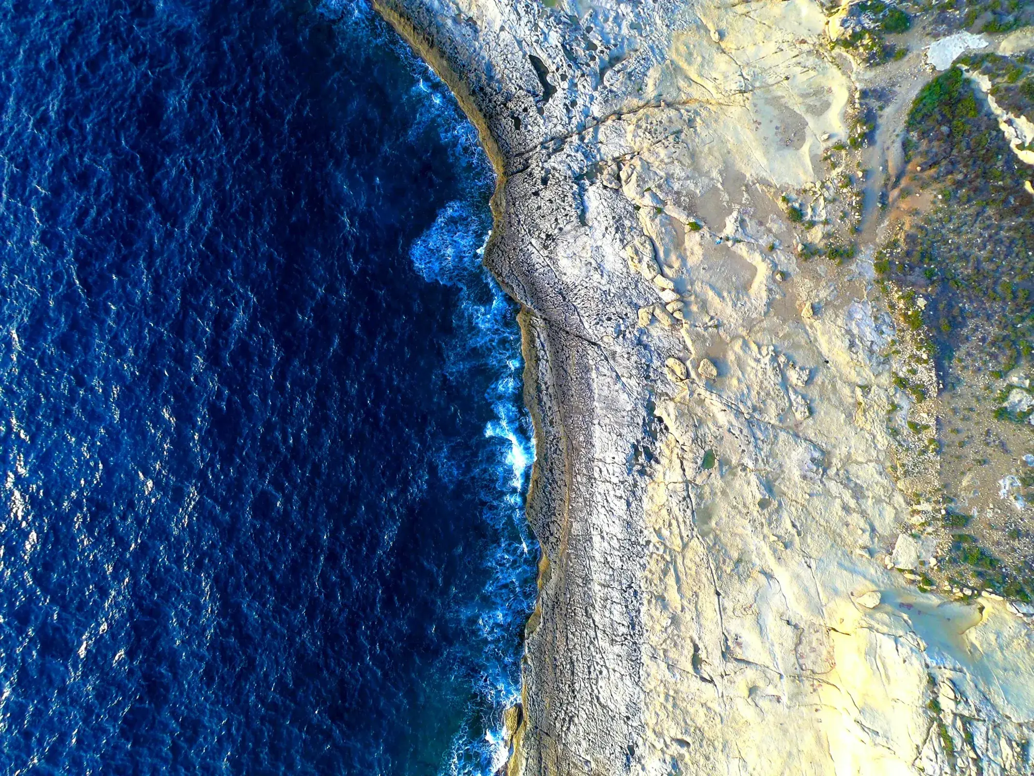Aerial view of deep blue water meeting Gozo's rocky shoreline